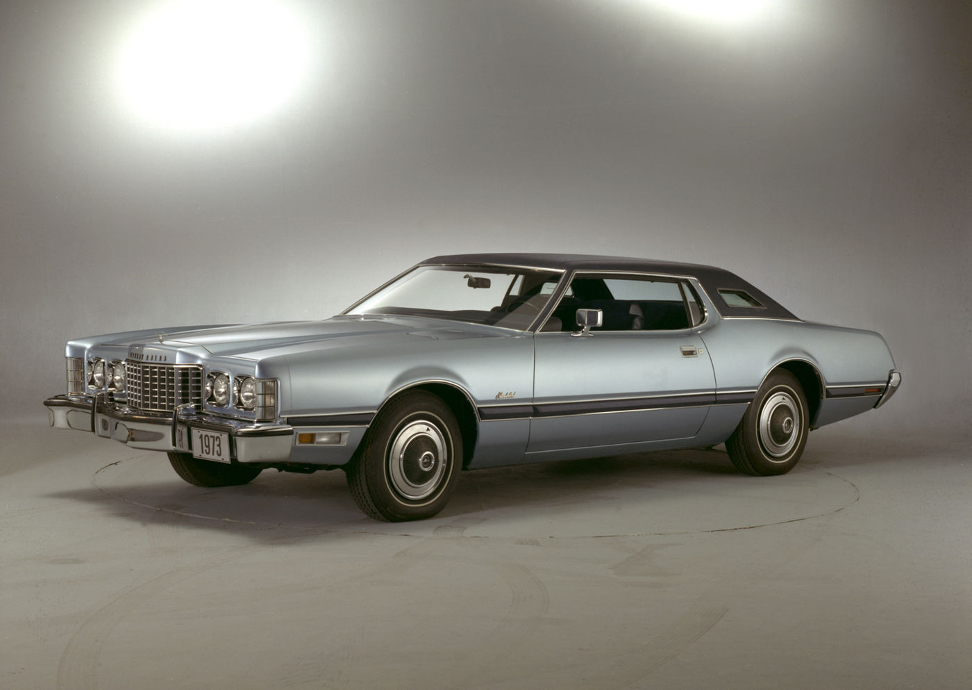 Light blue 1973 Ford Thunderbird two-door with a dark vinyl roof, front three-quarter studio view