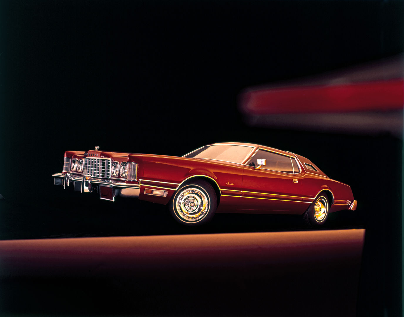 Red 1975 Ford Thunderbird two-door on a dark set with streaks of light, front three-quarter view