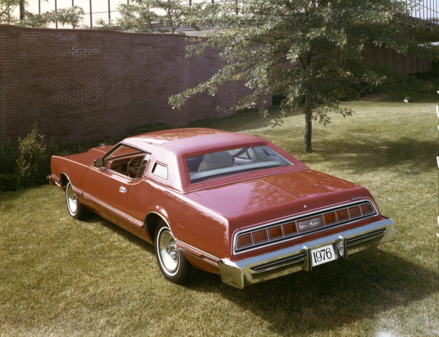 Red 1976 Ford Thunderbird two-door on grass by a brick wall, rear three-quarter view