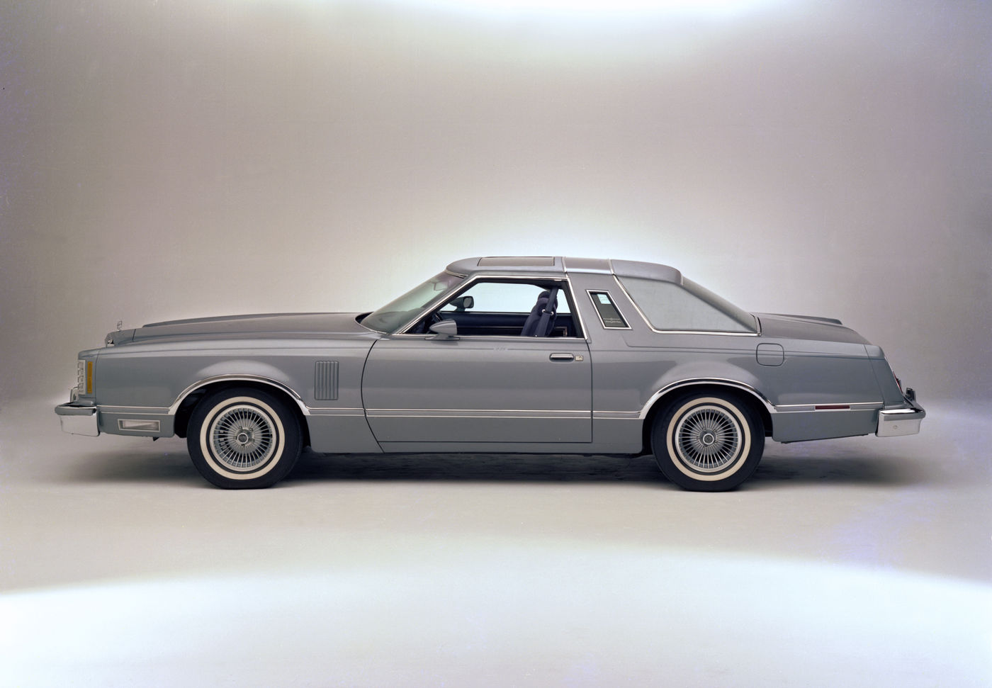 Silver-blue 1978 Ford Thunderbird Diamond Jubilee Edition in full side profile in a studio, with a padded roof and wire wheel covers