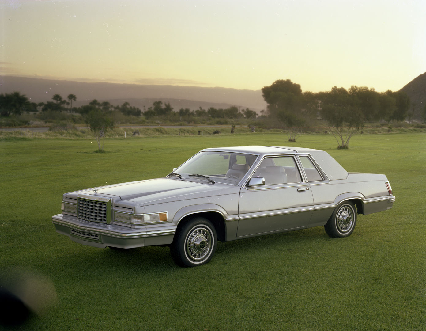 Two-tone silver 1980 Ford Thunderbird coupe on a lawn at dusk, front three-quarter view