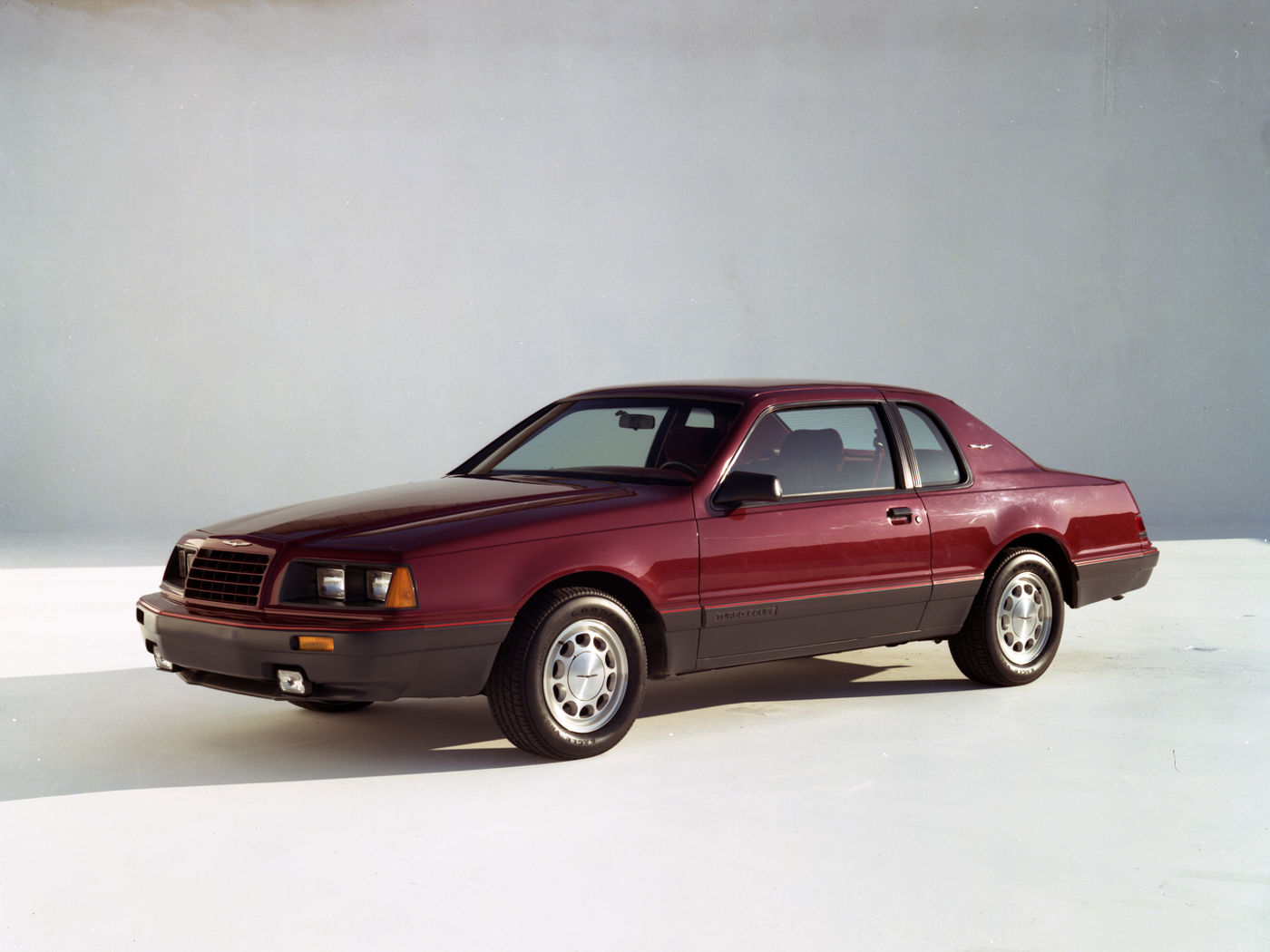 Dark red 1985 Ford Thunderbird Turbo Coupe with lower-body cladding and fog lamps, front three-quarter studio view