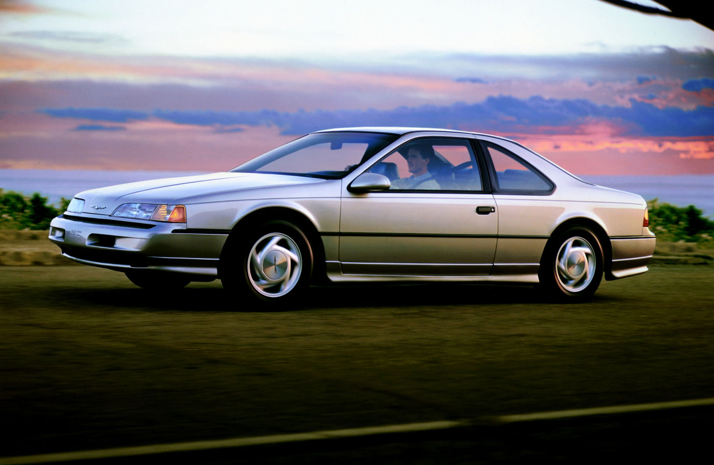 Silver 1991 Ford Thunderbird coupe on grass under a sunset sky, front three-quarter side view