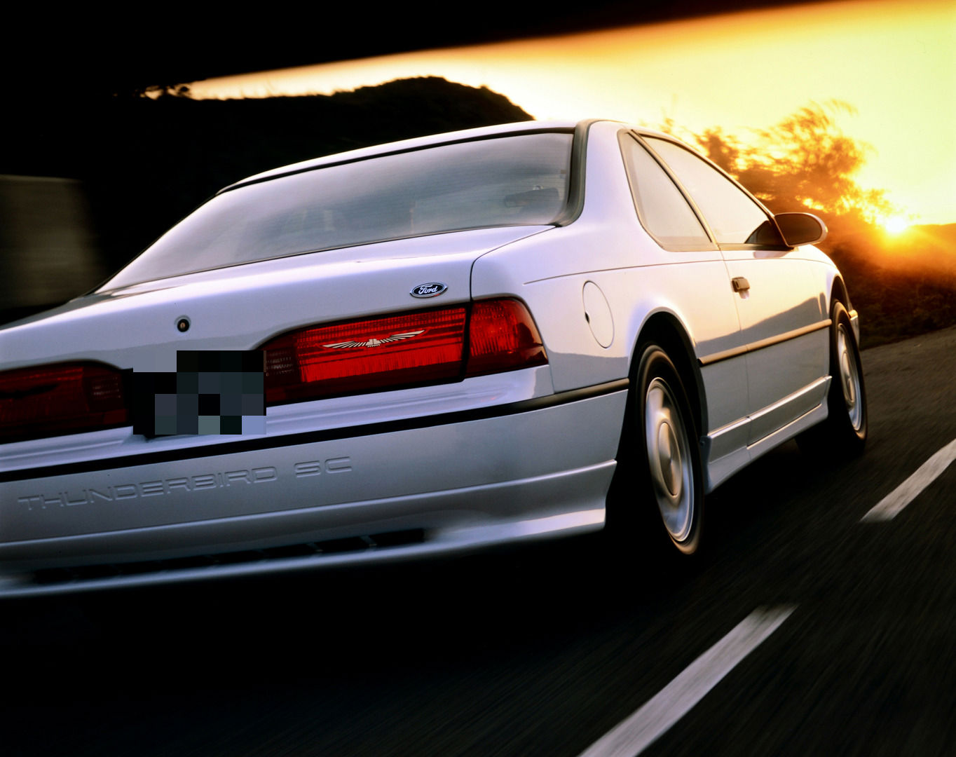 White 1992 Ford Thunderbird driving at sunset, close rear three-quarter view with THUNDERBIRD SC molded into the rear bumper