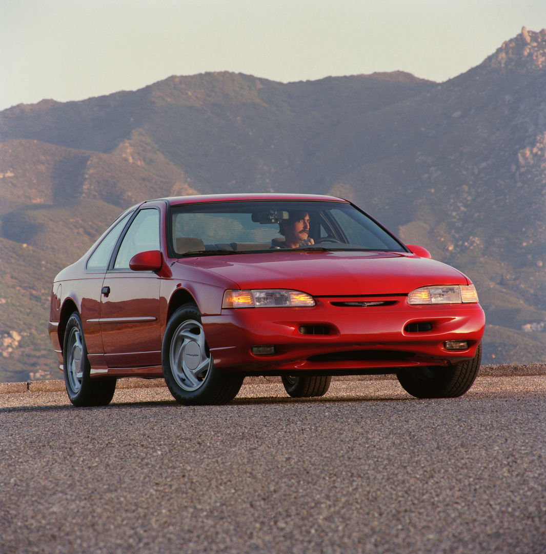 Red 1994 Ford Thunderbird Super Coupe with the restyled nose and lower grille, front three-quarter view before mountains
