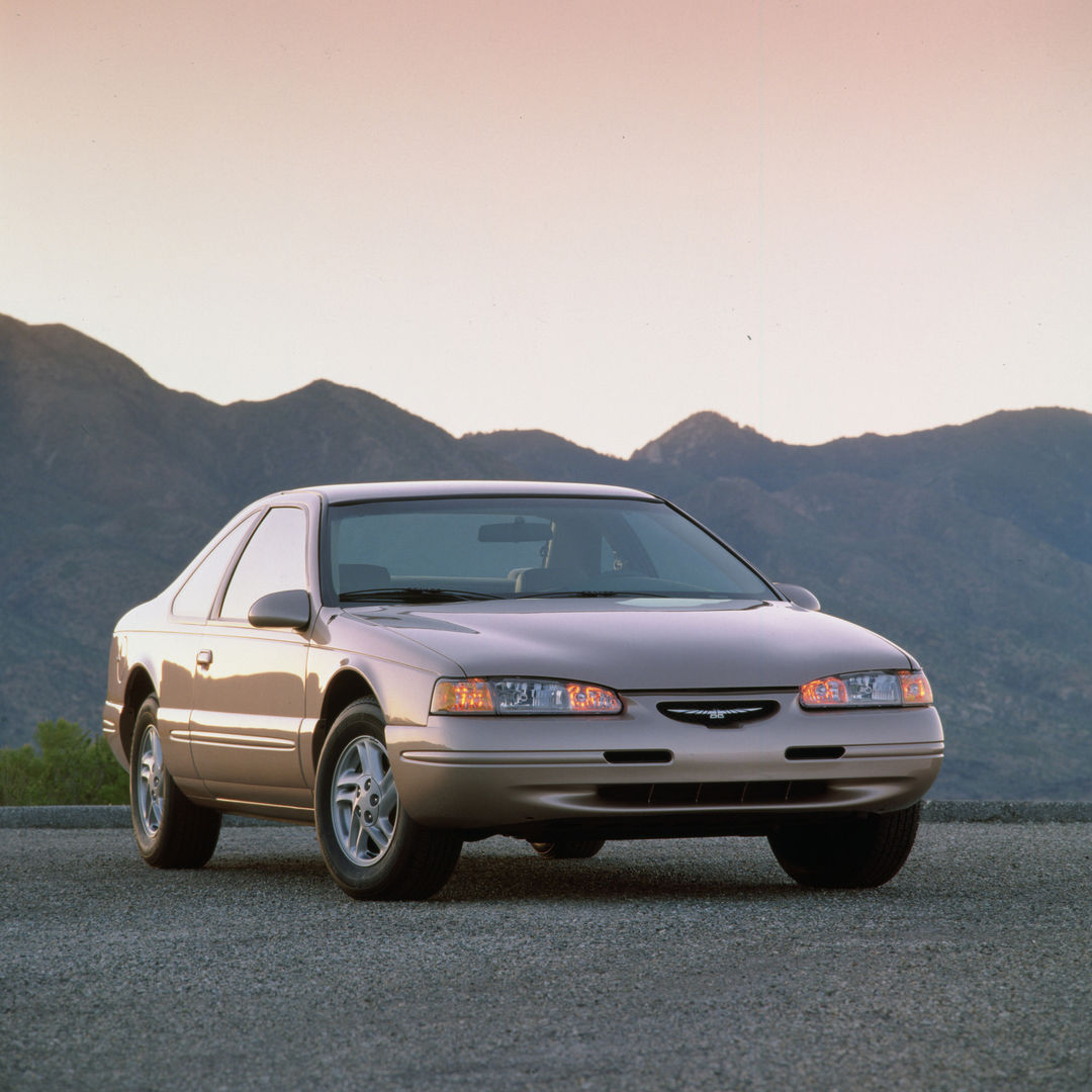 Taupe 1997 Ford Thunderbird LX coupe on a gravel lot below mountains, front three-quarter view