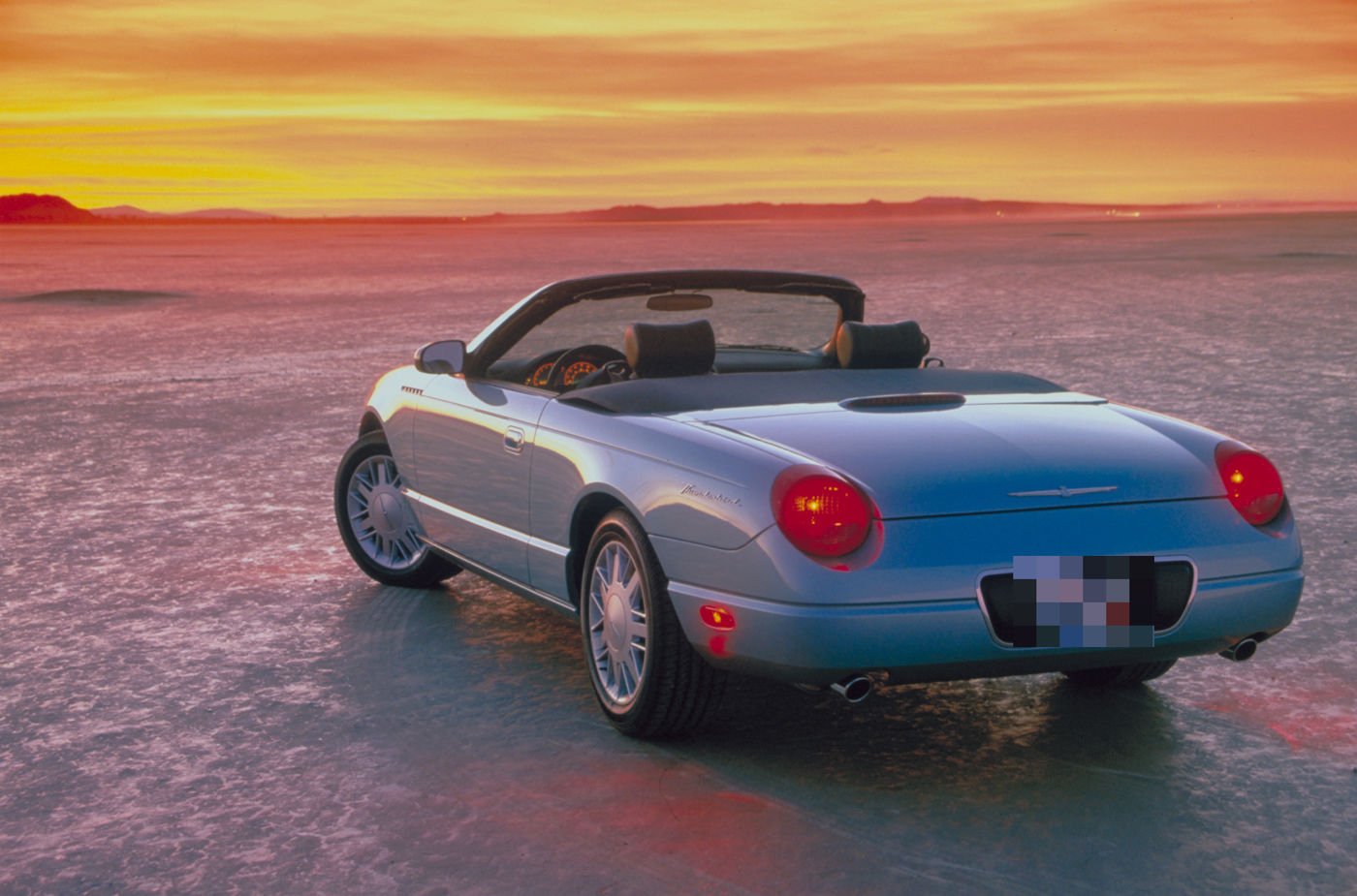 Light blue 2002 Ford Thunderbird two-seat convertible on a dry lakebed at sunset, rear three-quarter view