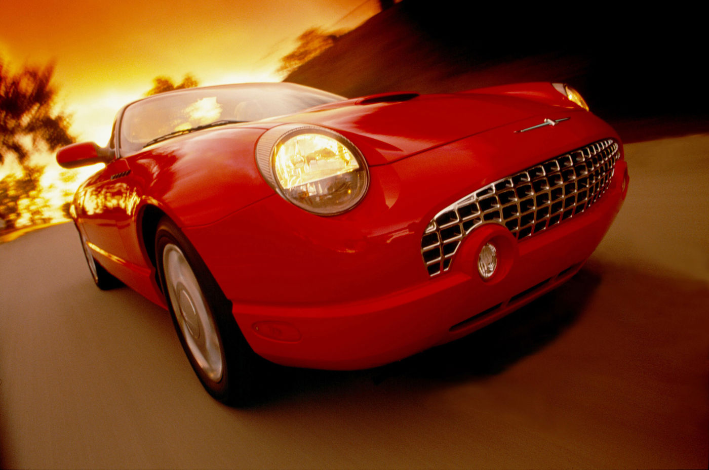 Red 2004 Ford Thunderbird photographed low and close in motion, showing the eggcrate grille and round headlamp