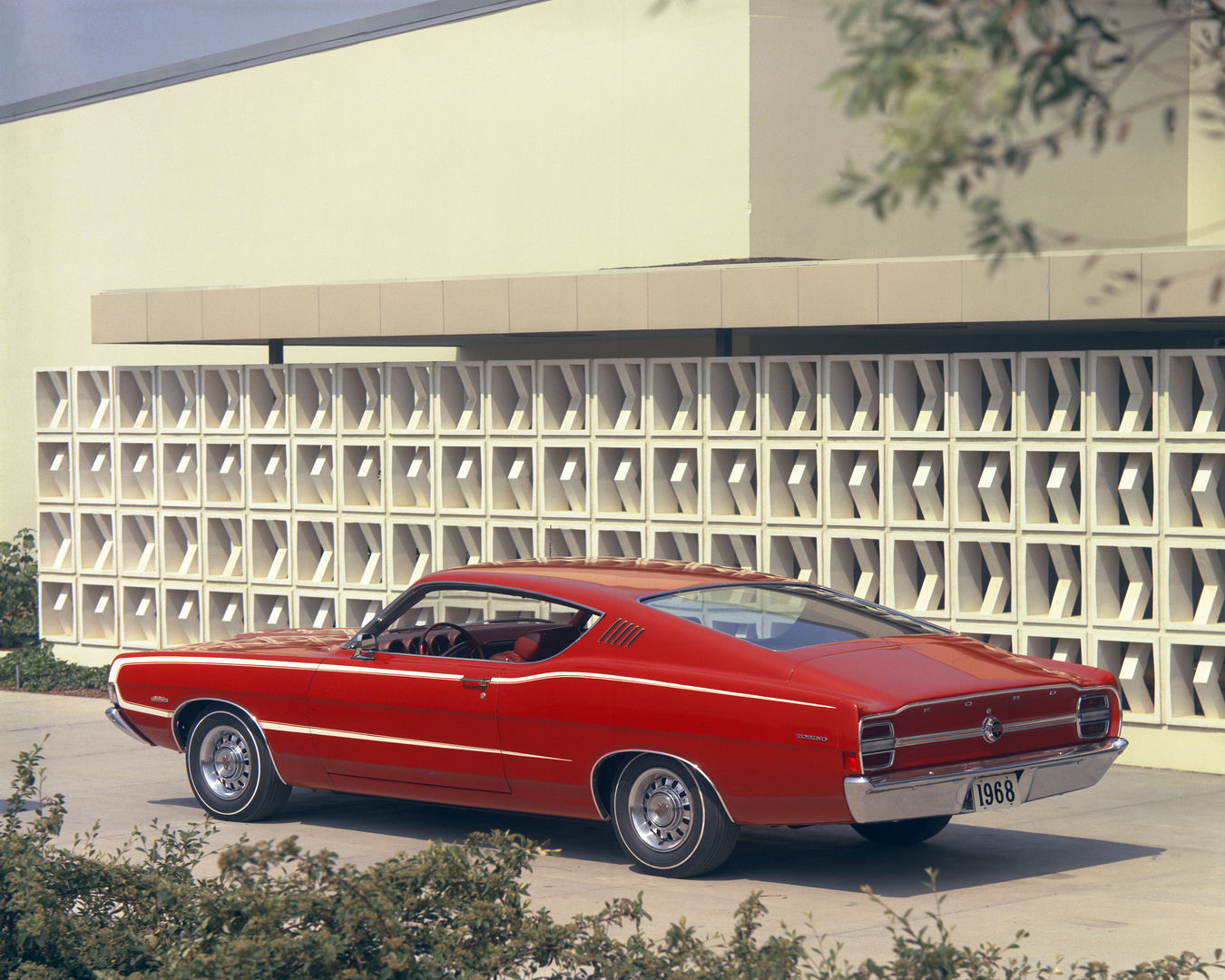 Red 1968 Ford Torino GT fastback seen from the rear three-quarter in front of a patterned concrete block wall, with a white body-side stripe
