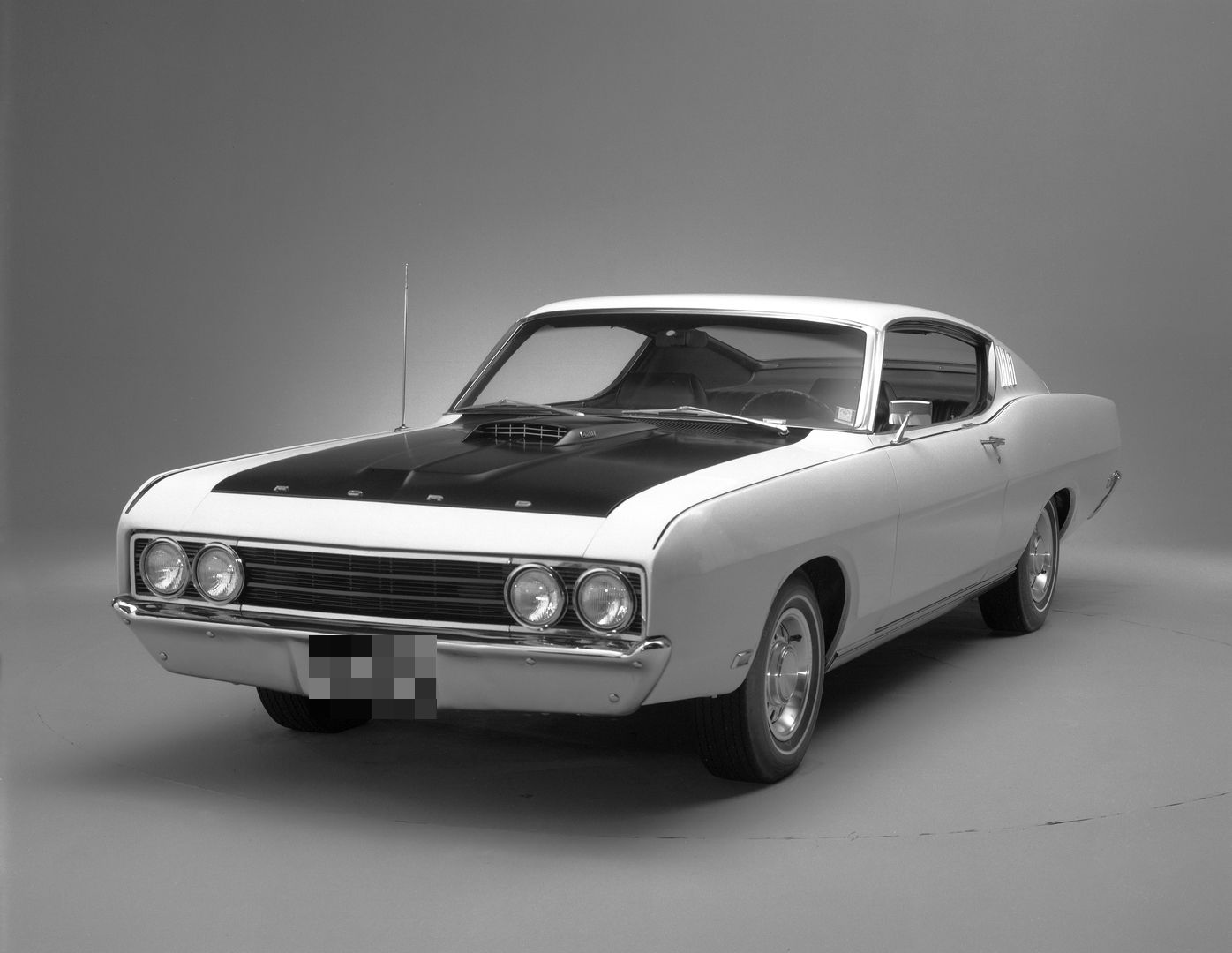 Black-and-white studio photo of a white 1969 Ford Torino Talladega with a black hood, front three-quarter view, showing the lengthened nose, flush grille and bumper