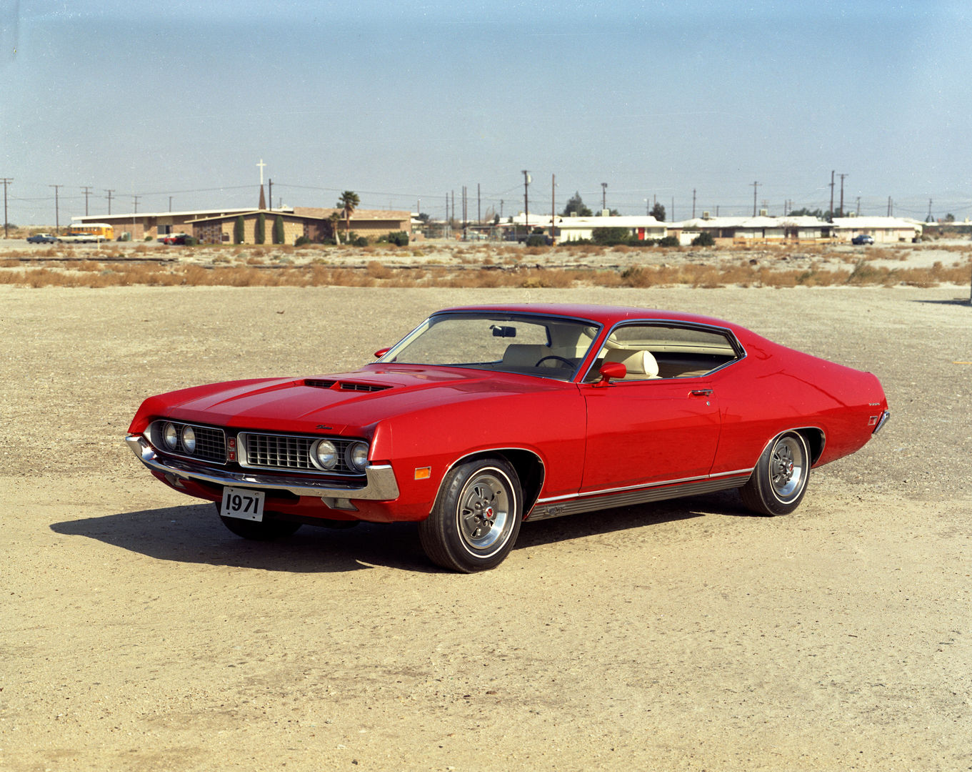 Red 1971 Ford Torino GT fastback with a white interior, front three-quarter view on a desert lot, showing the hood scoop and GT grille badge
