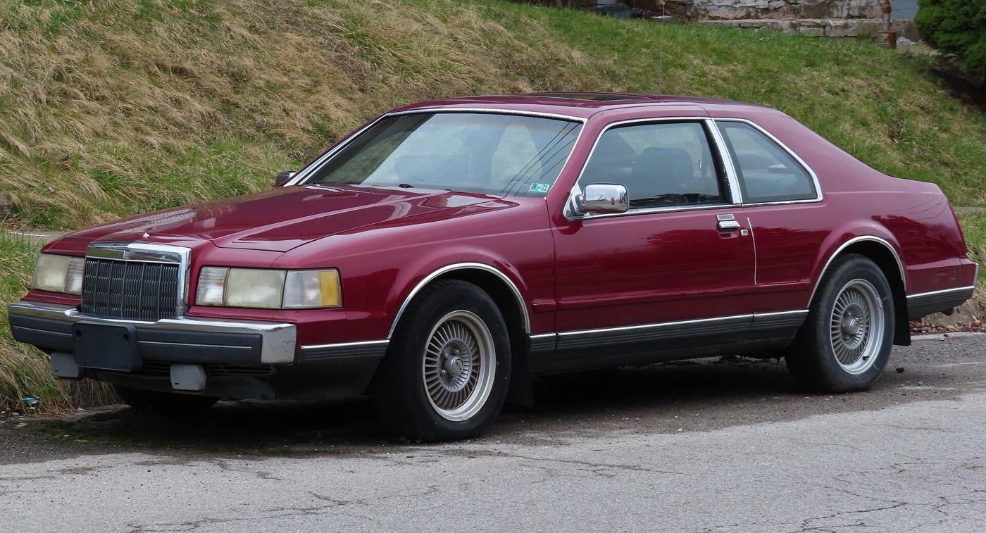 Dark red 1989 Lincoln Mark VII LSC two-door coupe parked by a grassy bank, front three-quarter view, with flush aero headlamps and multi-spoke alloy wheels
