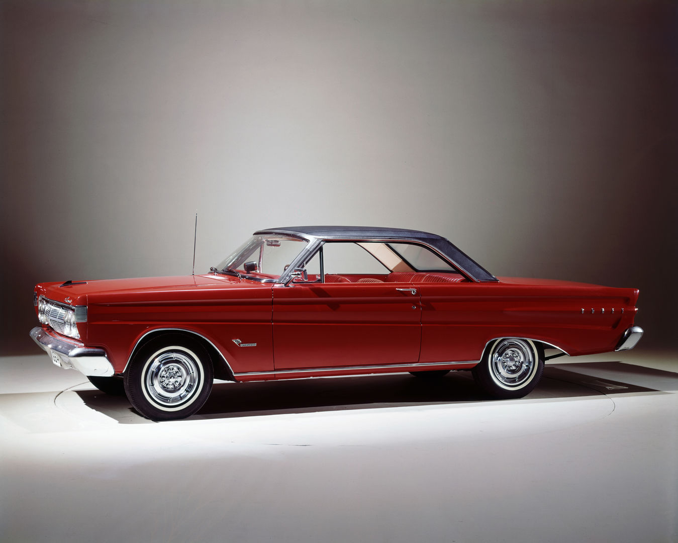 Red 1964 Mercury Comet Cyclone two-door hardtop with a black roof and chrome-look wheel covers, side and front three-quarter studio view