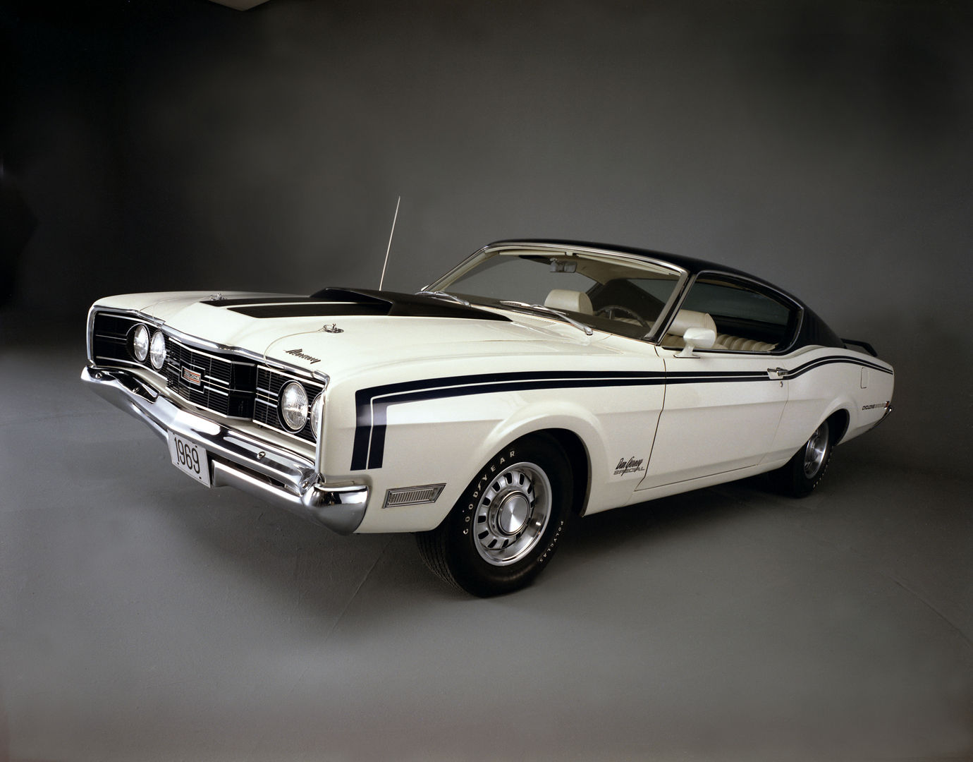 White 1969 Mercury Cyclone Spoiler with a dark blue roof, hood and body stripes and a Dan Gurney signature decal on the front fender, front three-quarter studio view