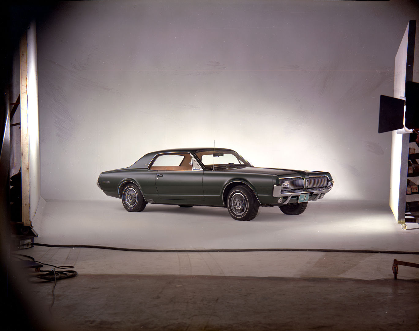 Dark green 1967 Mercury Cougar XR-7 hardtop on a curved studio scrim, with lights and set edges visible around it
