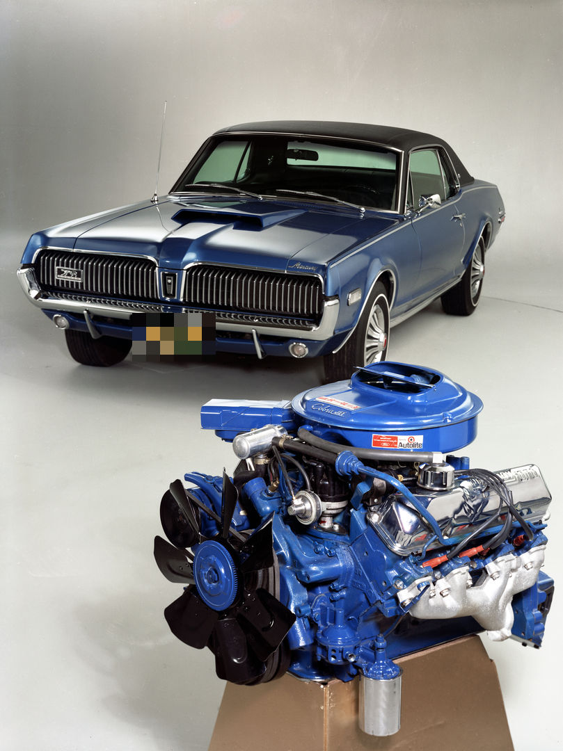 Studio composition of a blue 1968 Mercury Cougar hardtop with a hood scoop behind a blue-painted 428 Cobra Jet V8 on a stand