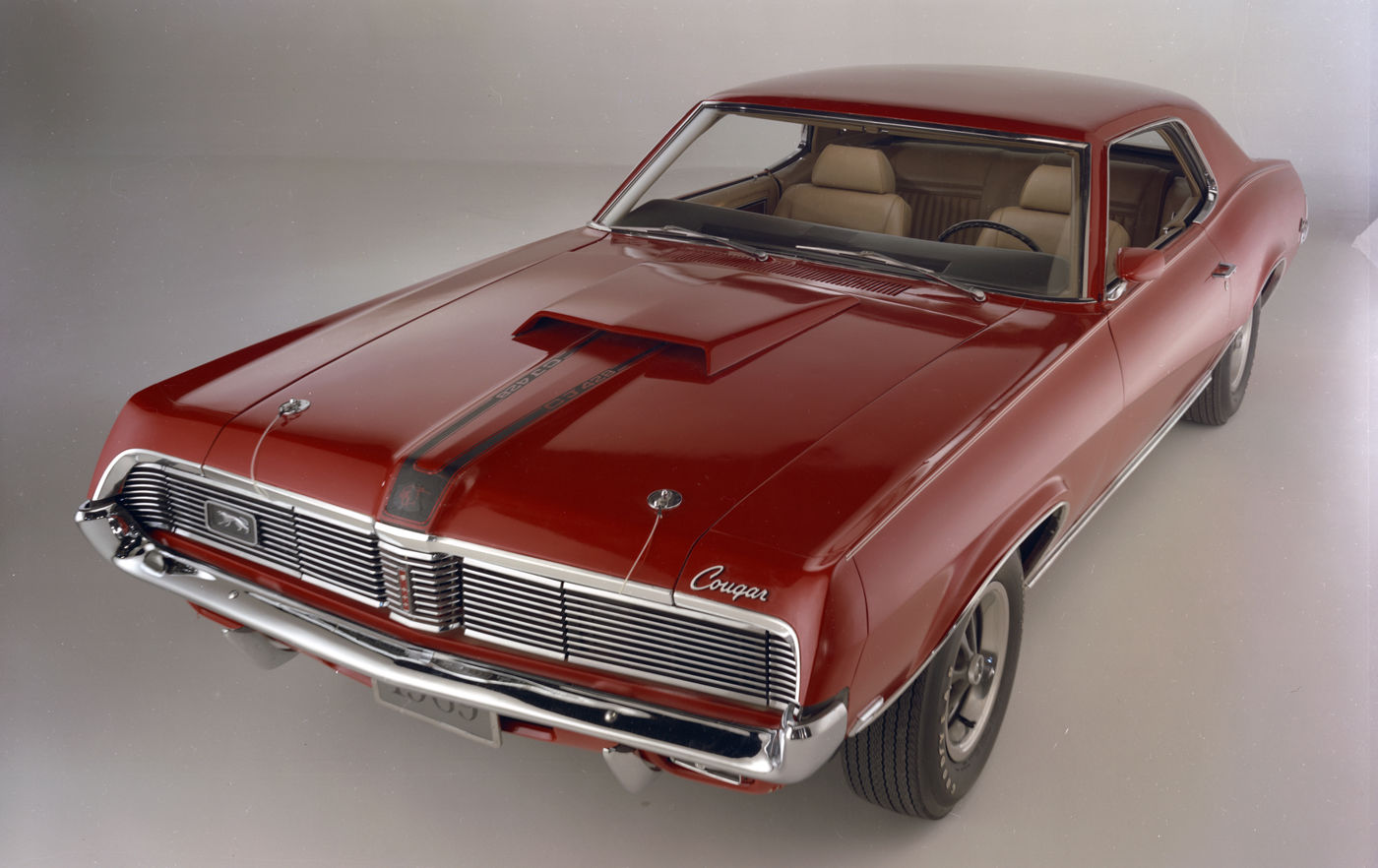 Dark red 1969 Mercury Cougar hardtop in a studio, high front three-quarter view, showing the functional hood scoop and the full-width grille with hidden headlights