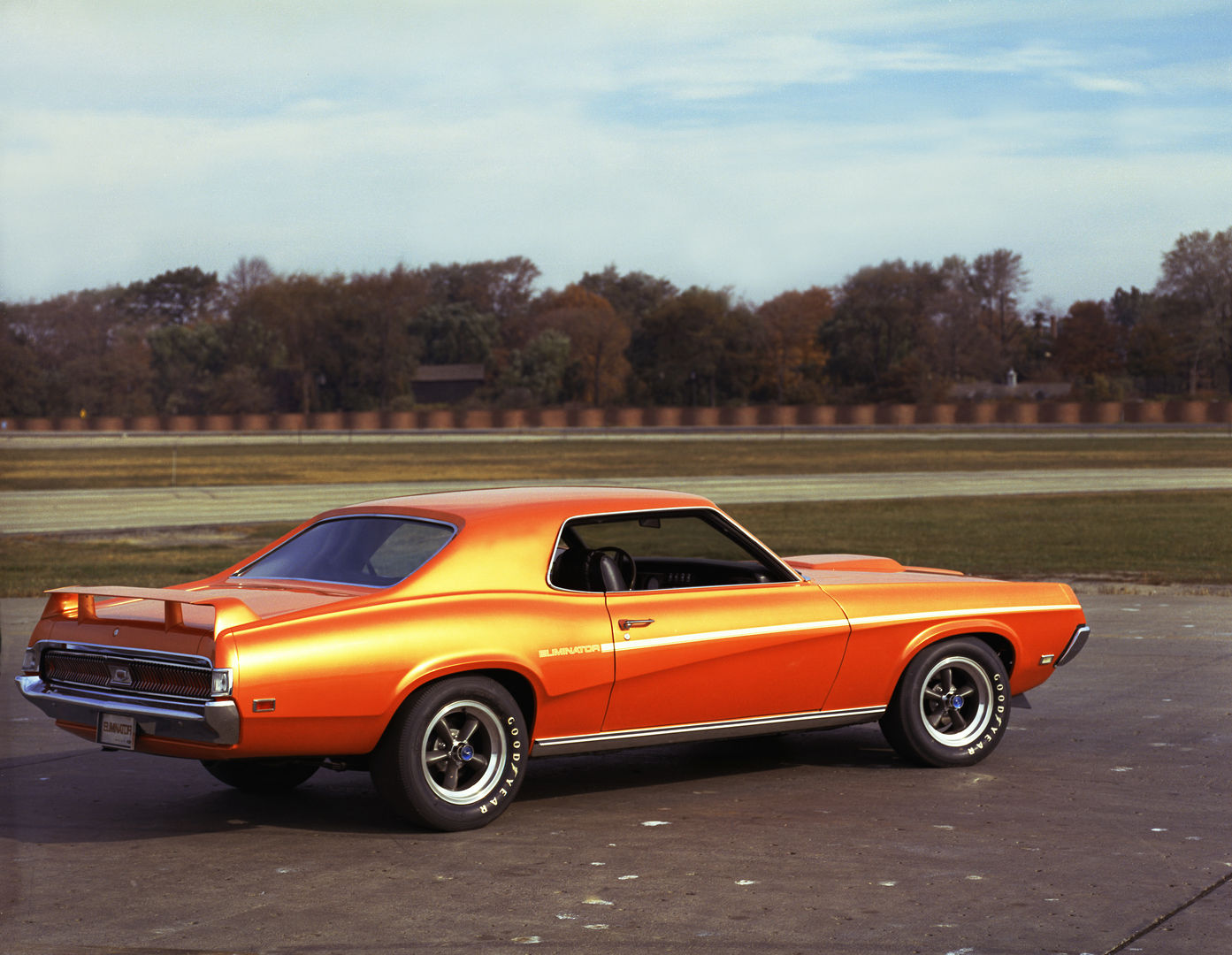Bright orange 1969 Mercury Cougar Eliminator hardtop on a test-track apron, rear three-quarter view, with a black side stripe, rear spoiler and styled wheels