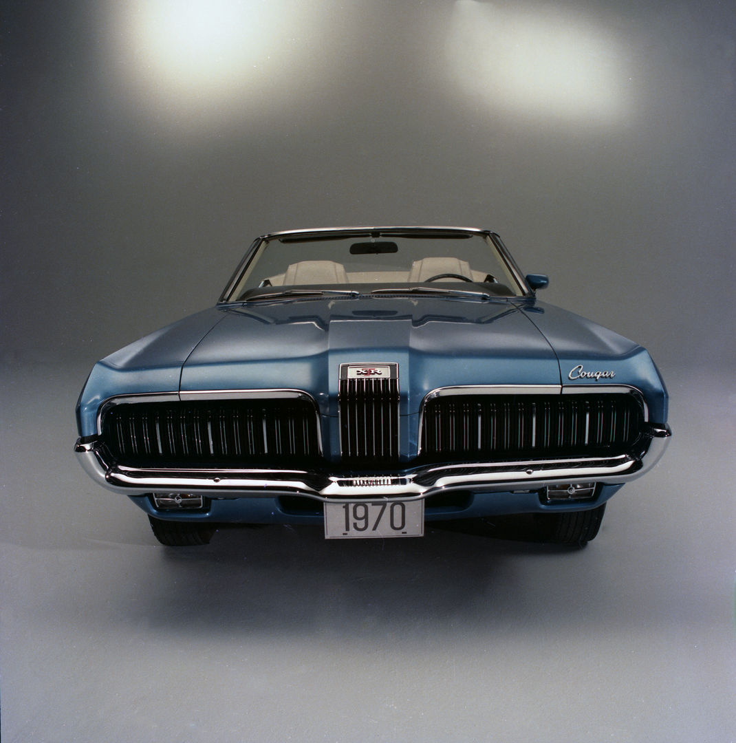 Blue 1970 Mercury Cougar XR-7 convertible seen head-on in a studio, showing the 1970 split grille with its vertical-bar center section