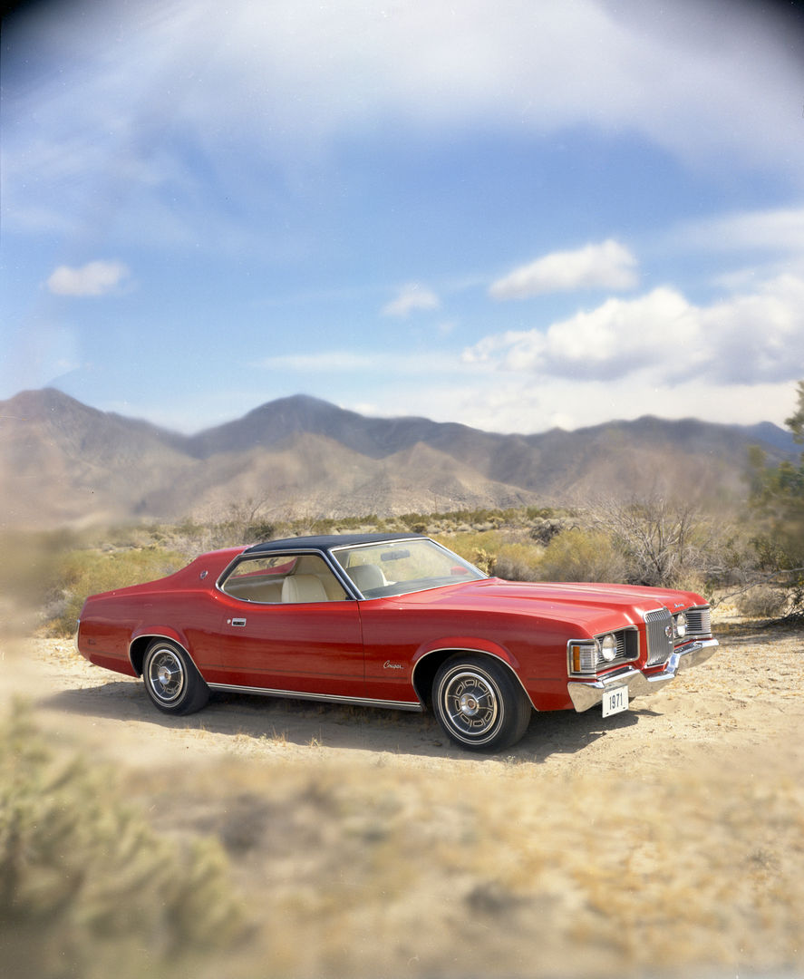 Red 1971 Mercury Cougar hardtop with a black vinyl roof on desert scrub below mountains, front three-quarter view