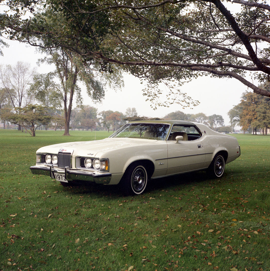 White 1973 Mercury Cougar XR-7 hardtop on a lawn under a spreading tree, front three-quarter view, with the larger 1973 front bumper