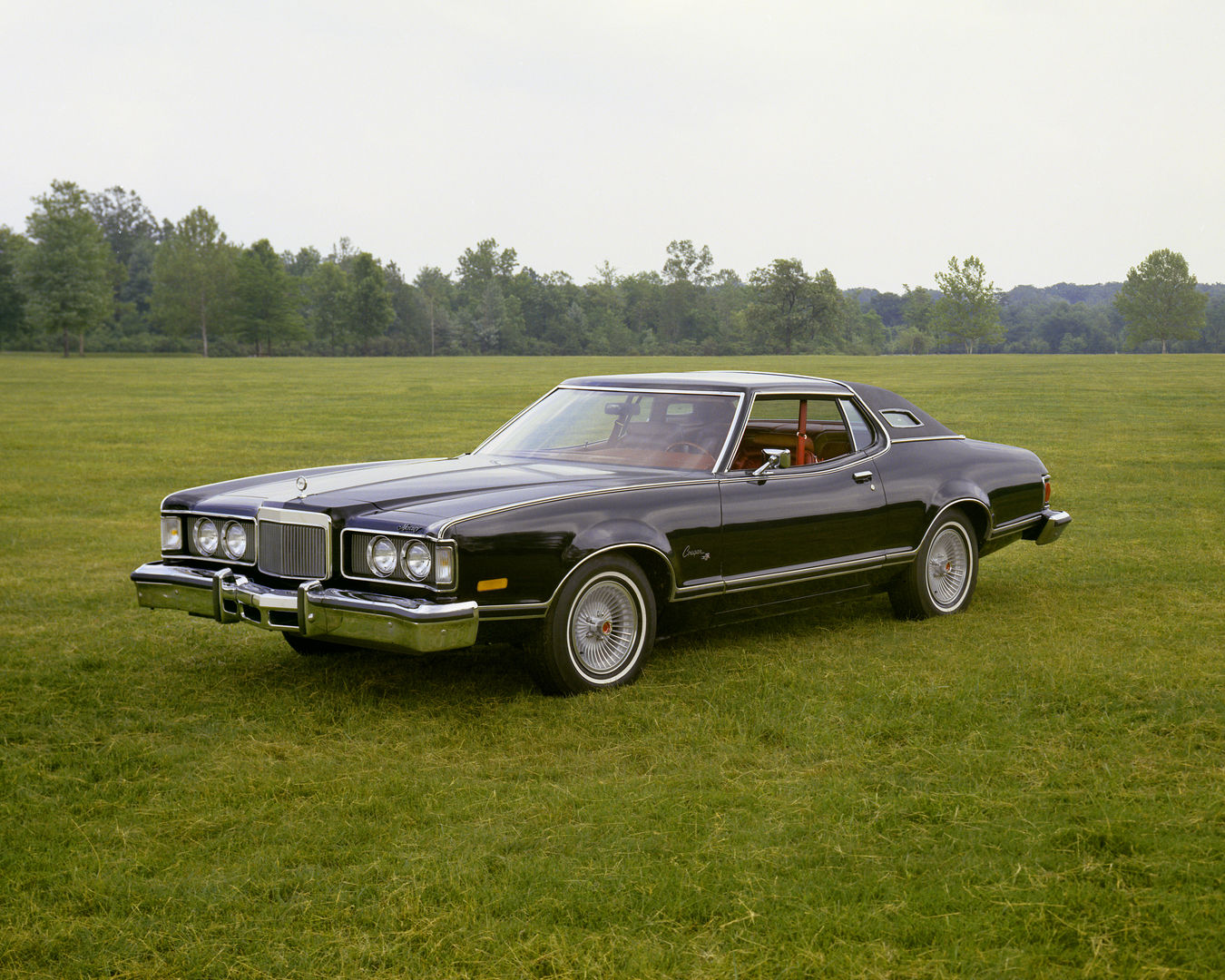 Black 1976 Mercury Cougar XR-7 on a grass field, front three-quarter view, with opera windows and wire wheel covers