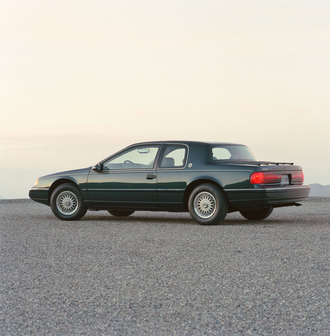 Dark green 1992 Mercury Cougar 25th Anniversary edition coupe, rear three-quarter view on gravel at dusk