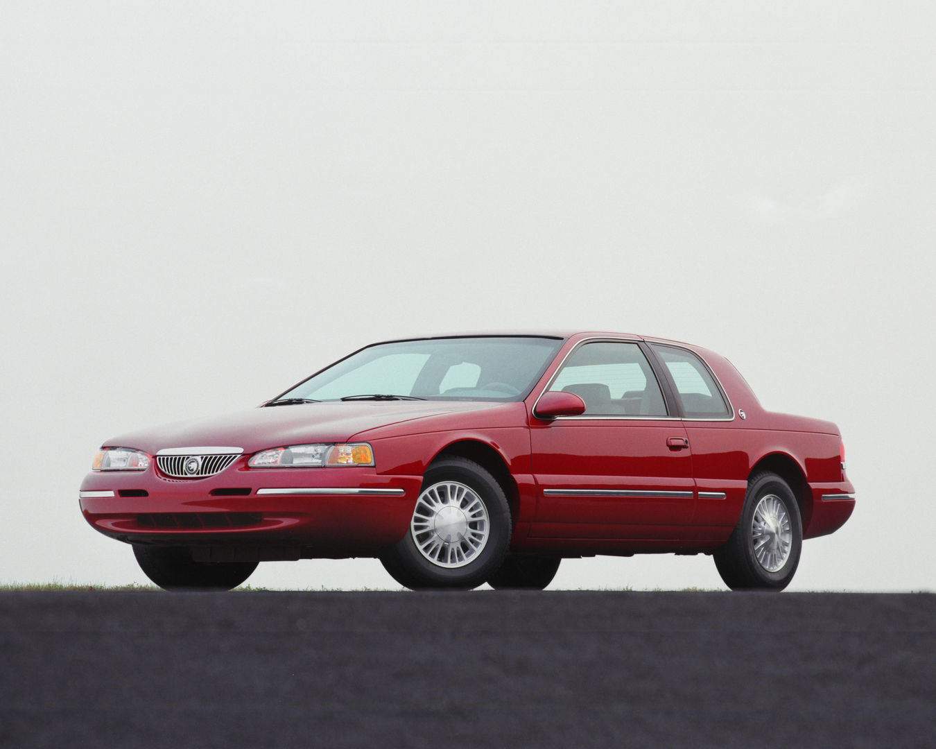 Red 1996 Mercury Cougar coupe with multi-spoke wheel covers, front three-quarter view against a pale sky