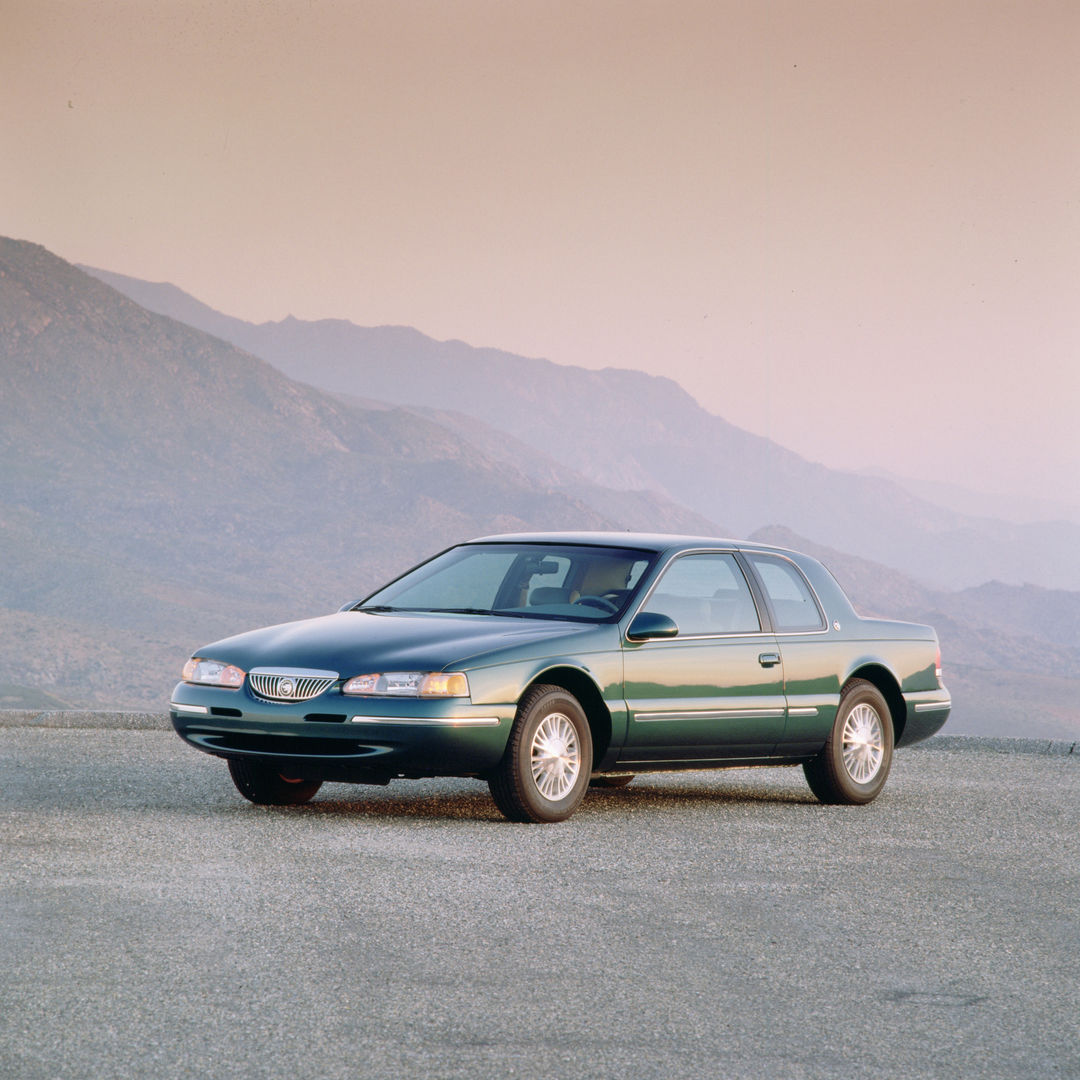 Dark green 1997 Mercury Cougar XR-7 coupe on a paved lot in front of pink-lit mountains, front three-quarter view