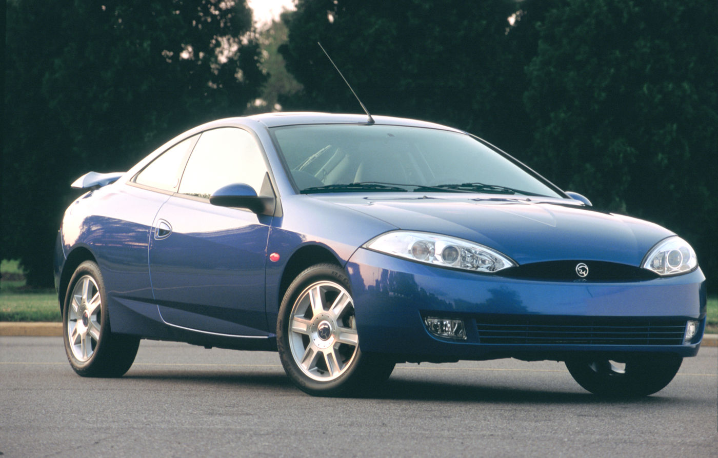 Blue 2001 Mercury Cougar hatchback coupe with a rear spoiler on a parking area among trees, front three-quarter view