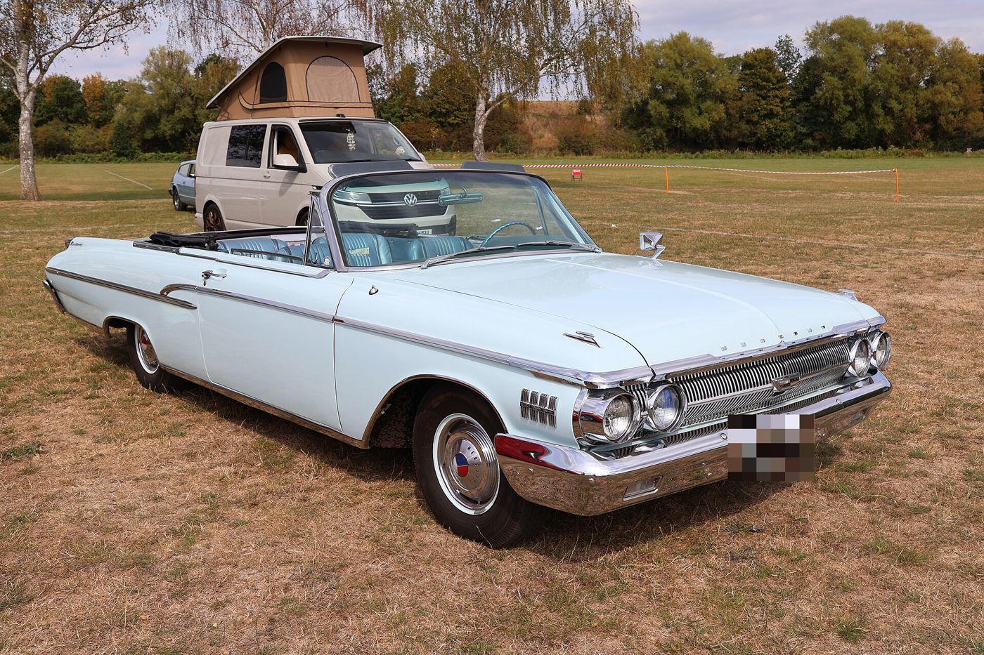 Pale blue 1962 Mercury Monterey S-55 convertible with the top down at an outdoor car show, front three-quarter view, with a blue bucket-seat interior
