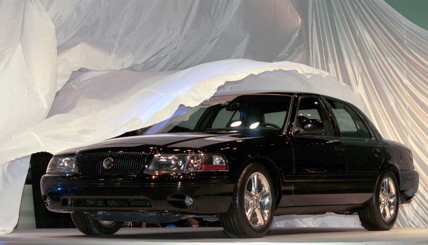 Black 2003 Mercury Marauder sedan emerging from under a white drape at its unveiling, front three-quarter view showing the monochrome grille and five-spoke wheels