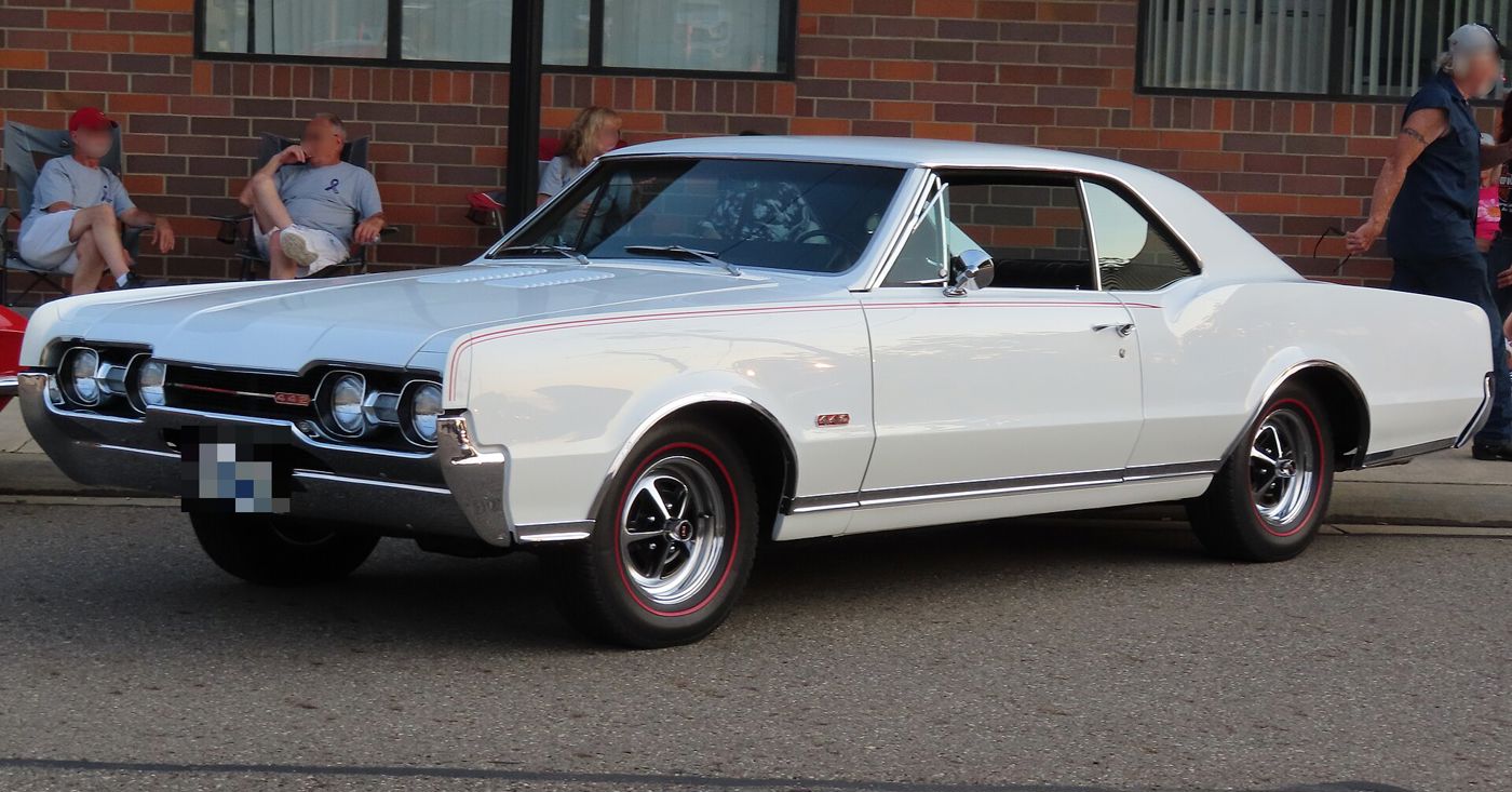 White 1967 Oldsmobile 4-4-2 Holiday coupe with red-line tires, front three-quarter, at a car show