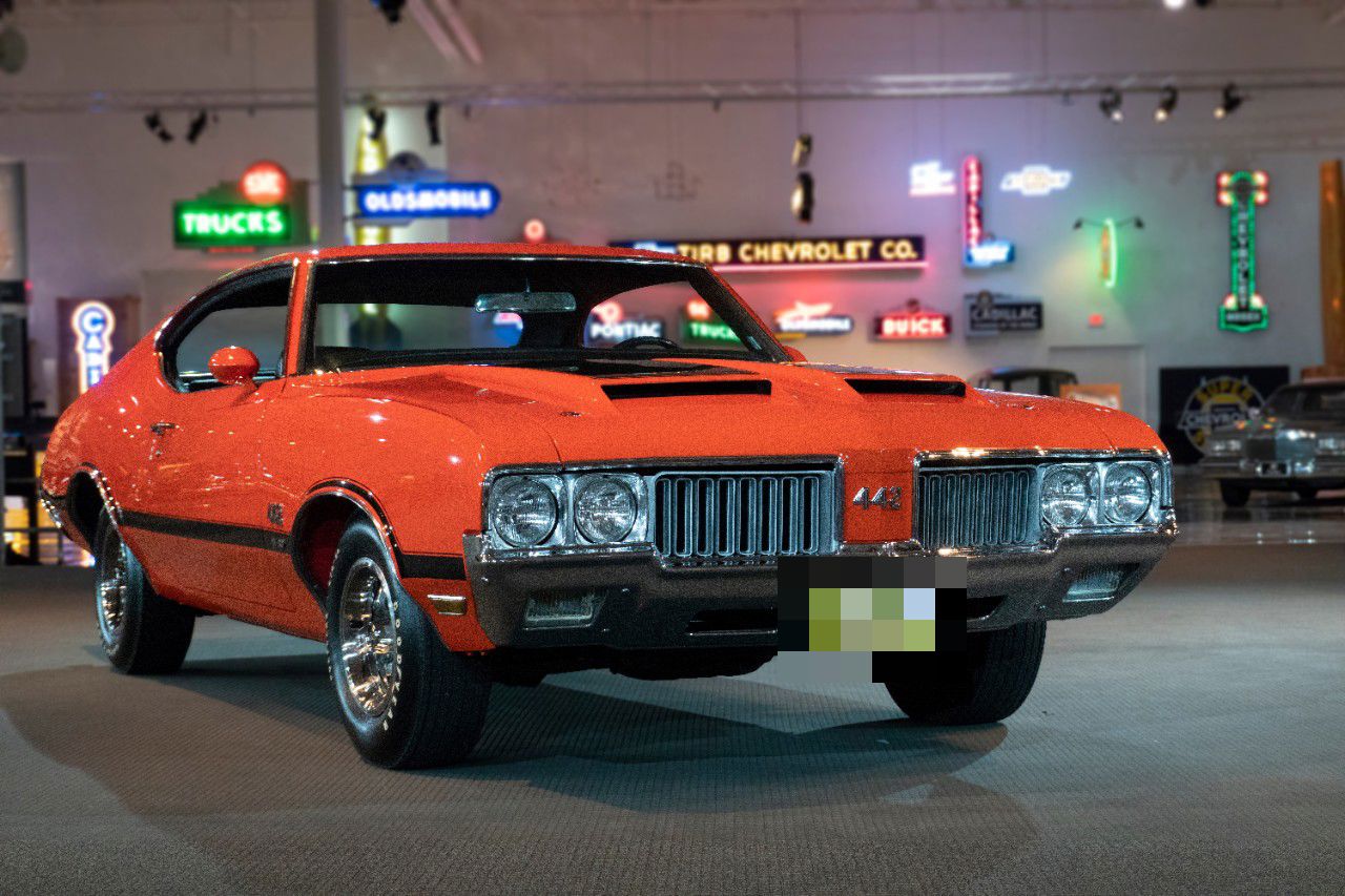 Orange 1970 Oldsmobile 4-4-2 W-30 hardtop with black stripes and hood scoops, front three-quarter, in a museum hall
