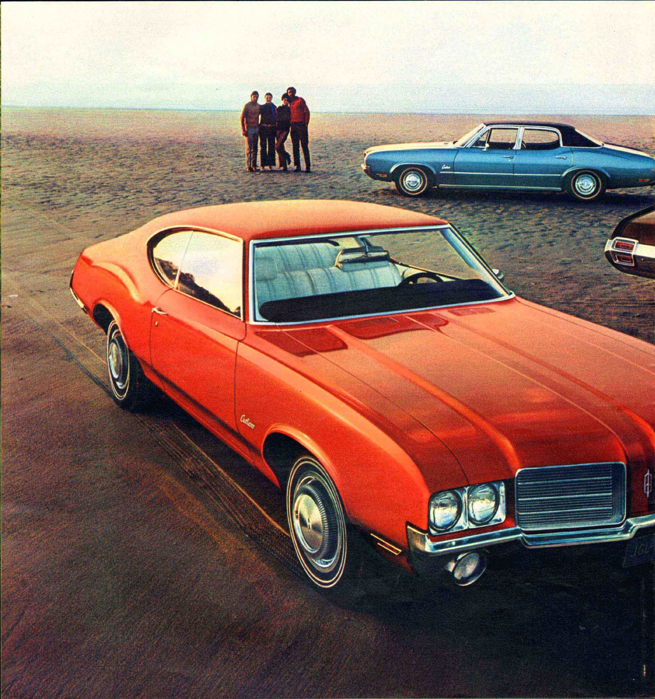 Brochure page: orange-red 1971 Cutlass hardtop coupe, front three-quarter, on a beach with a blue Cutlass behind