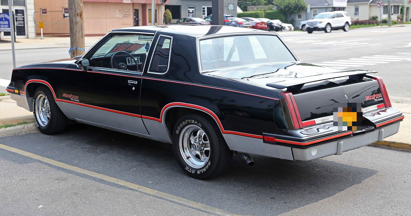 Black-and-silver 1983 Hurst/Olds from the rear three-quarter, with red striping and spoiler