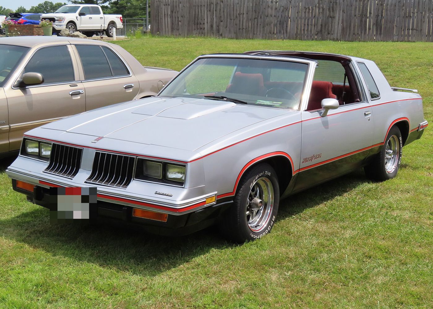Silver-and-black 1984 Hurst/Olds coupe with T-tops, front three-quarter, on grass