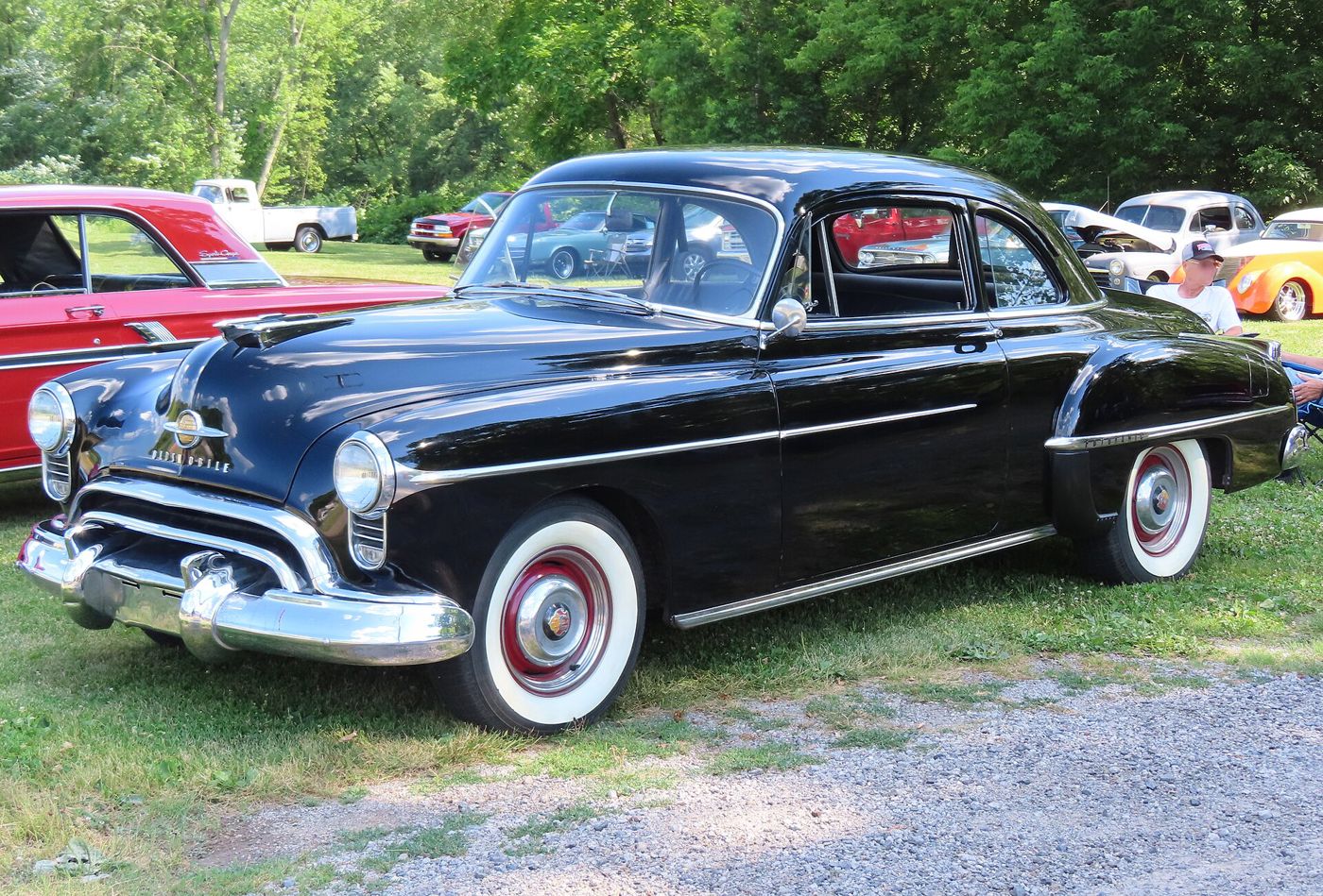 Black 1950 Oldsmobile Futuramic 88 club coupe with whitewall tires, front three-quarter, on grass at a car show