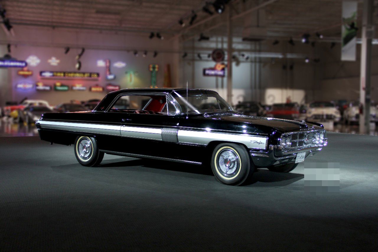 Black 1962 Oldsmobile Starfire hardtop coupe with its brushed-aluminum side panel, front three-quarter, in a museum hall