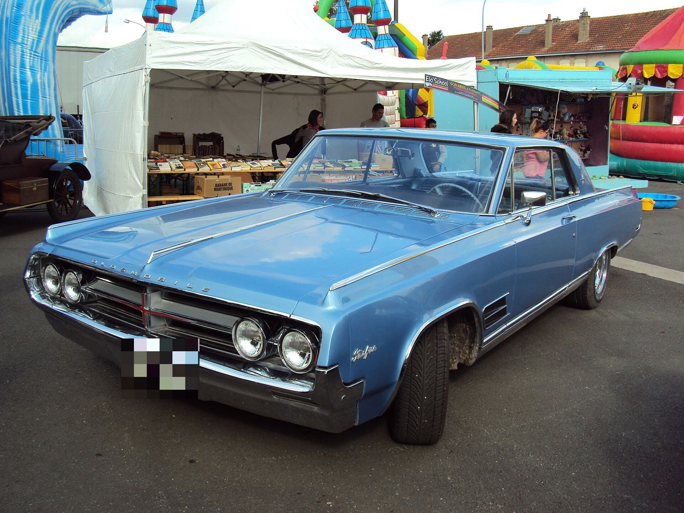 Light-blue 1964 Oldsmobile Starfire hardtop coupe, front three-quarter, at a fair