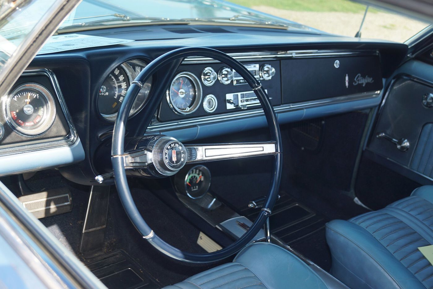 Blue interior of a 1965 Oldsmobile Starfire: steering wheel, gauges and dash with Starfire script