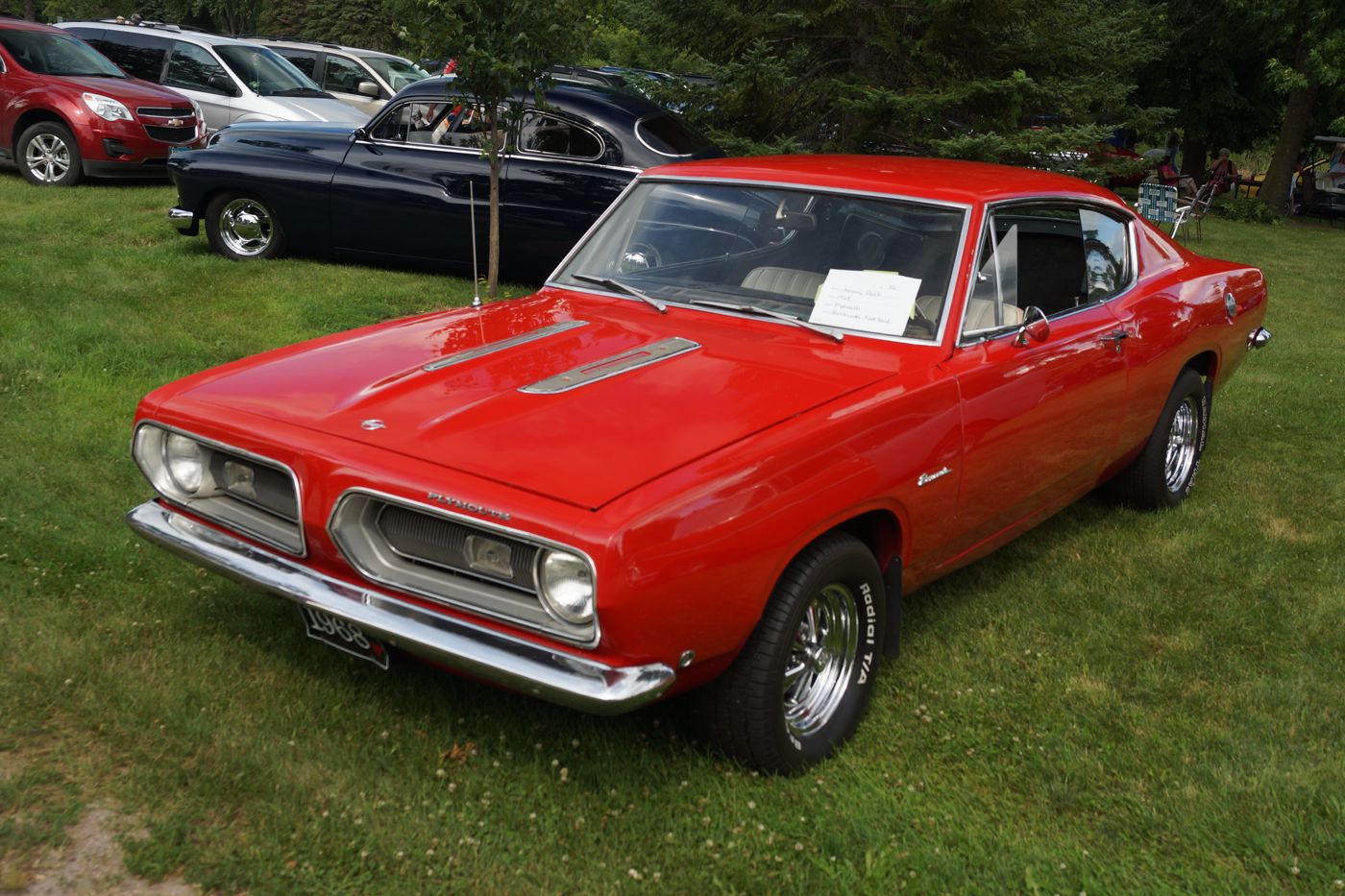 Red 1968 Plymouth Barracuda hardtop on grass, front three-quarter, with the split grille and hood louvres