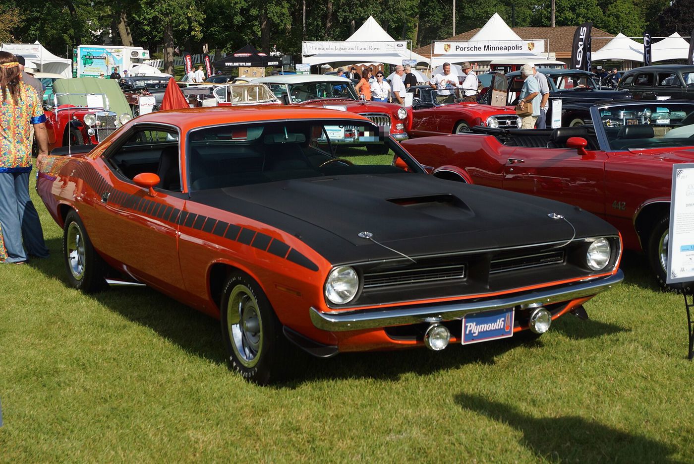 Orange 1970 Plymouth AAR Cuda with a matte-black hood, black strobe side stripe and AAR badge, on grass at a show