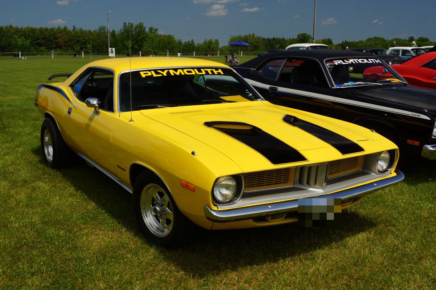 Yellow 1974 Plymouth Cuda with black hood stripes and PLYMOUTH windshield banner, front three-quarter