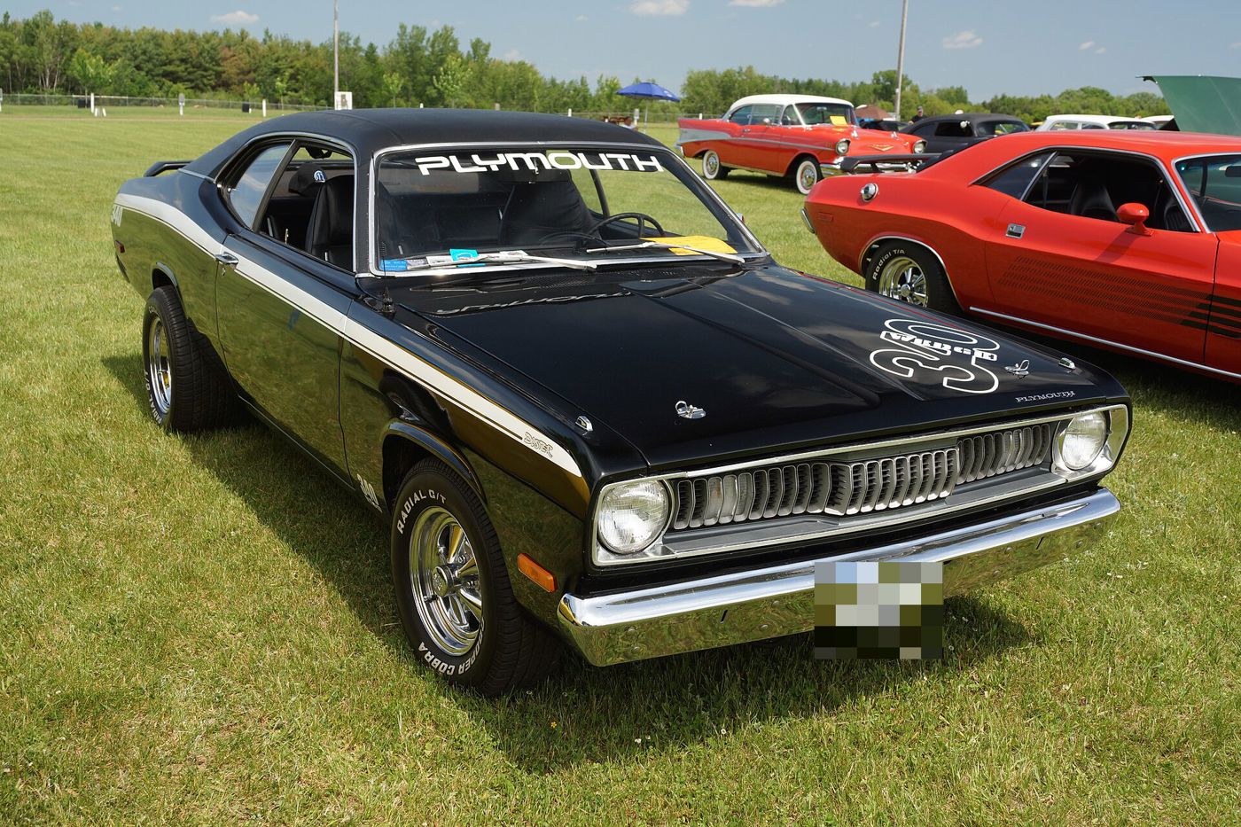 Black 1972 Plymouth Duster with a white side stripe and hood decal, PLYMOUTH windshield banner, front three-quarter on grass