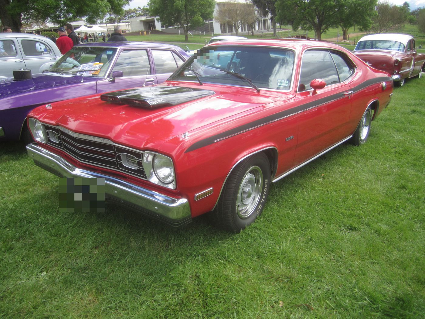 Red 1973 Plymouth Duster 340 with black side stripe and twin hood scoops, front three-quarter on grass