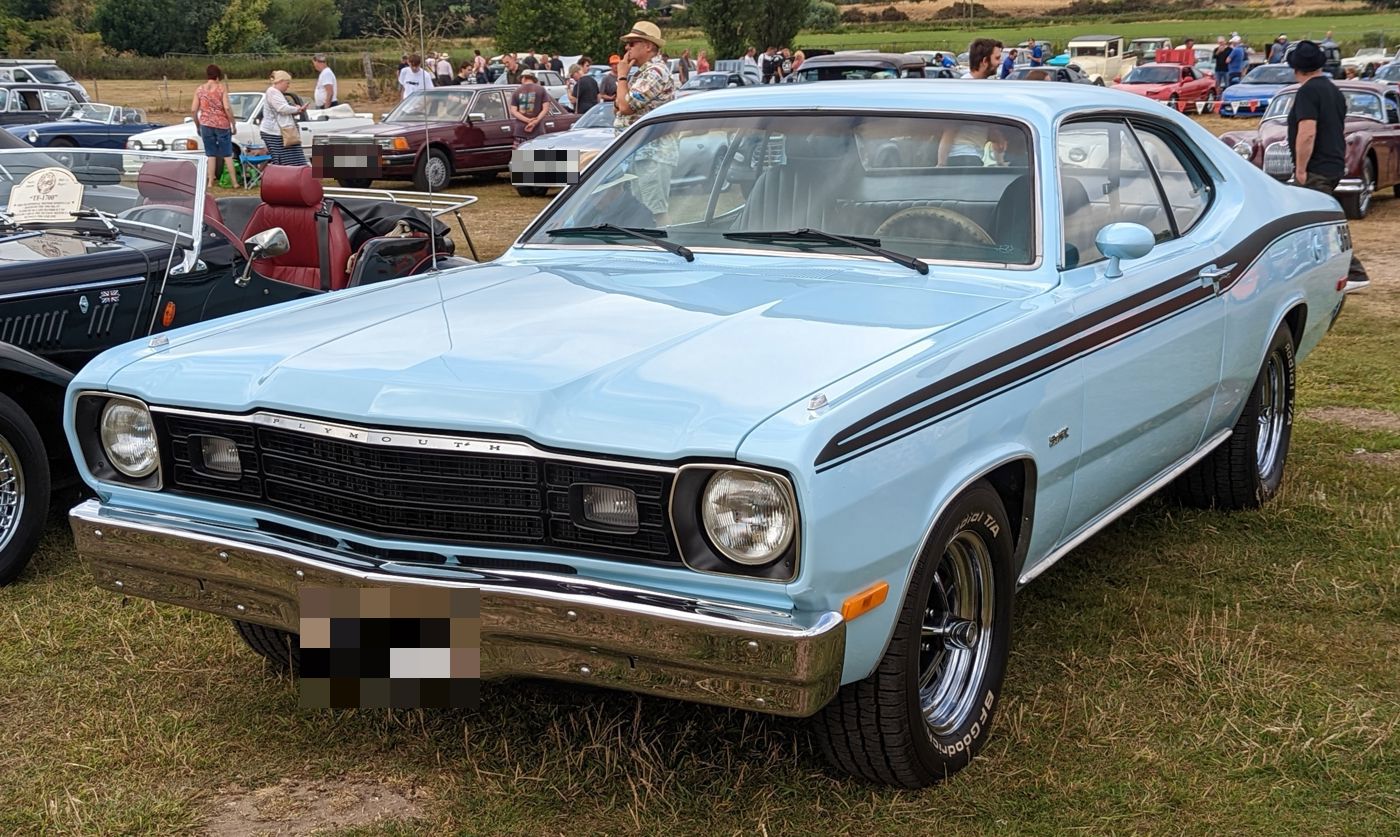 Light blue 1974 Plymouth Duster with dark tape stripes along the flanks, front three-quarter at a UK show
