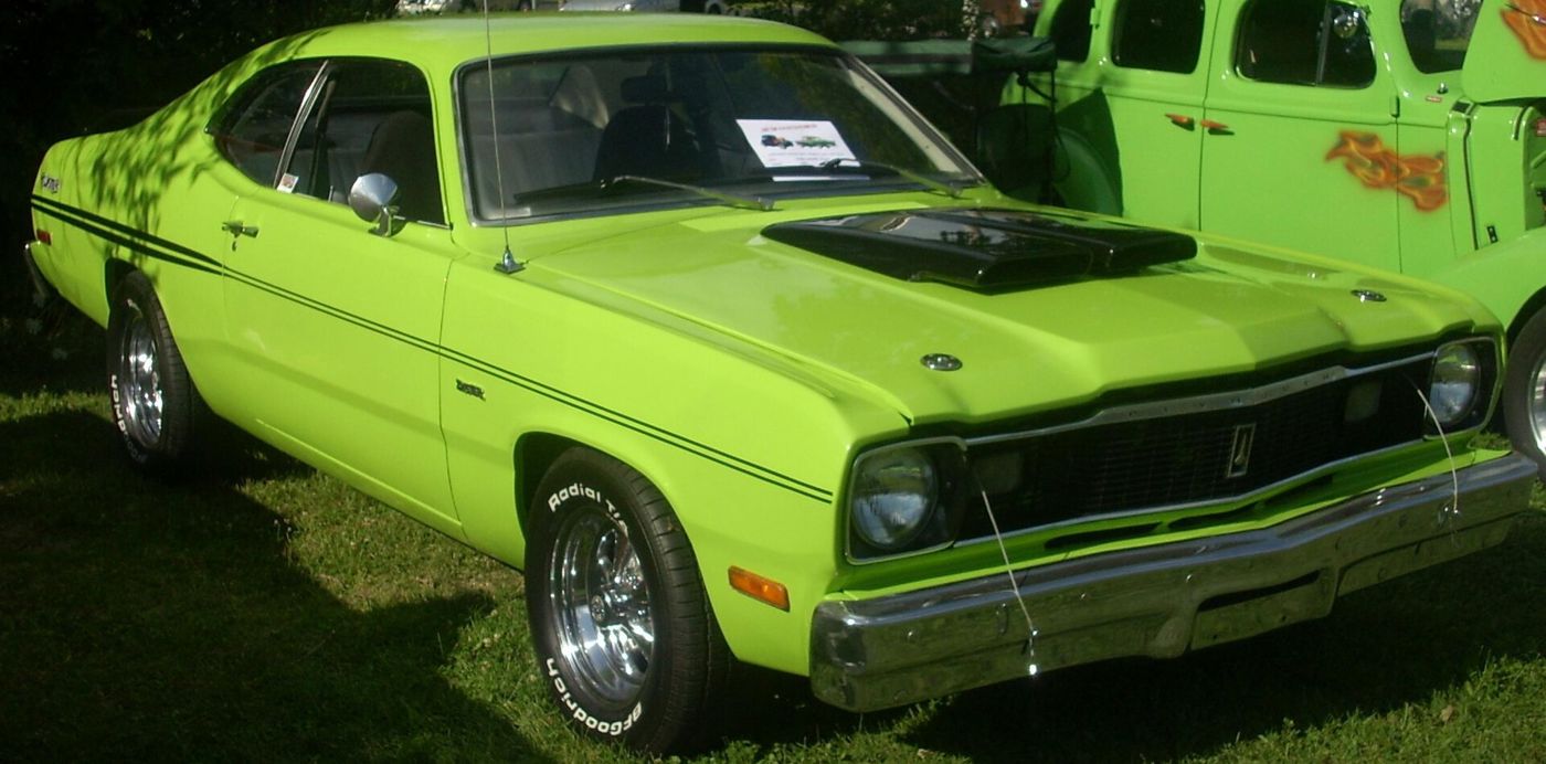 Lime green 1975 Plymouth Duster with black hood panel and side pinstripes, seen close from the front three-quarter