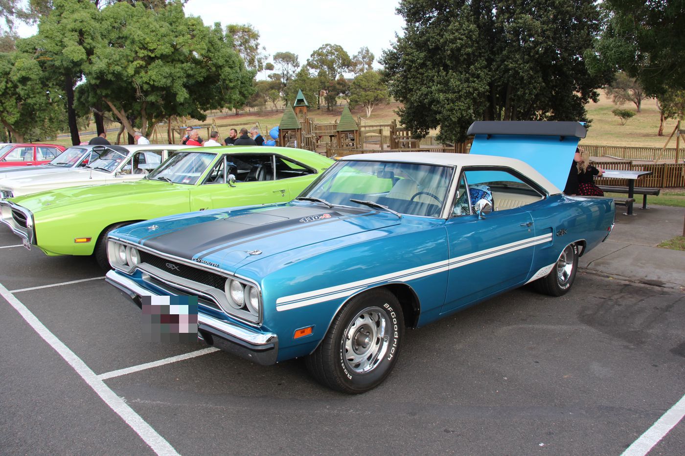 Blue 1970 Plymouth GTX with white roof and reflective side stripe, front three-quarter in a car park