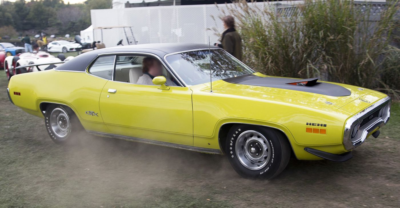 Curious Yellow 1971 Plymouth GTX with black vinyl roof and HEMI fender callout, driving across grass